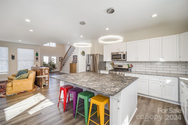 kitchen featuring stainless steel appliances, white cabinets, dark hardwood / wood-style floors, hanging light fixtures, and a breakfast bar area