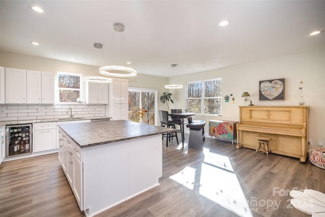 kitchen with white cabinetry, a center island, beverage cooler, decorative light fixtures, and hardwood / wood-style flooring