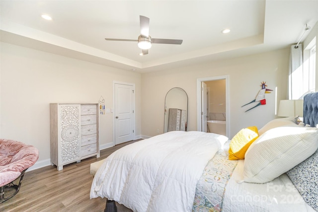 bedroom featuring ceiling fan, light hardwood / wood-style floors, connected bathroom, and a tray ceiling