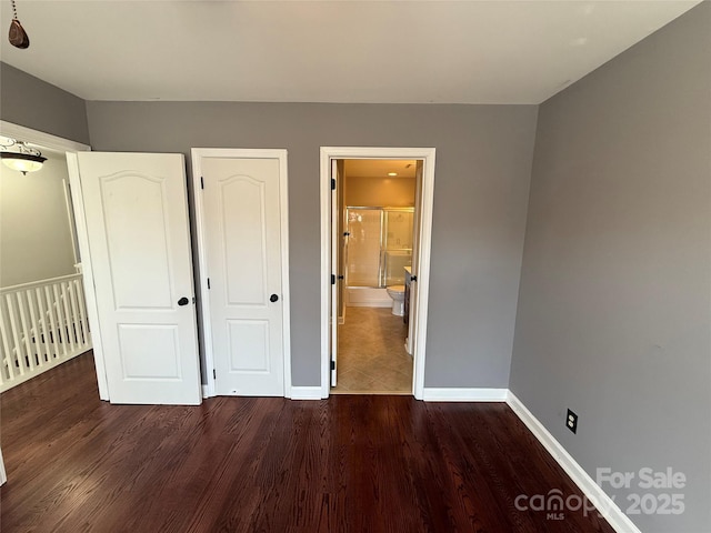 unfurnished bedroom featuring connected bathroom, baseboards, and wood finished floors