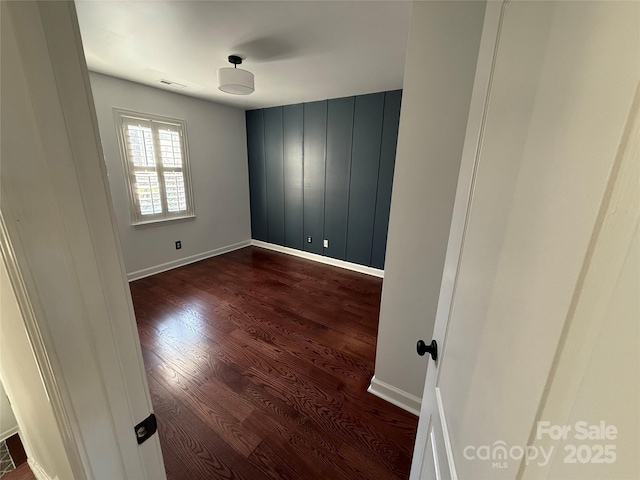 unfurnished room with baseboards, visible vents, and dark wood-style flooring