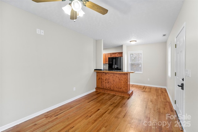 interior space featuring ceiling fan, black refrigerator, light wood-type flooring, and a textured ceiling