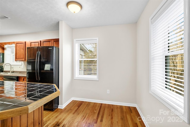 kitchen featuring black refrigerator, sink, tile countertops, light hardwood / wood-style flooring, and dishwasher