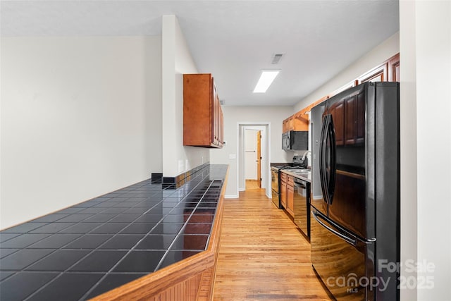 kitchen with tile countertops, light hardwood / wood-style flooring, and black appliances