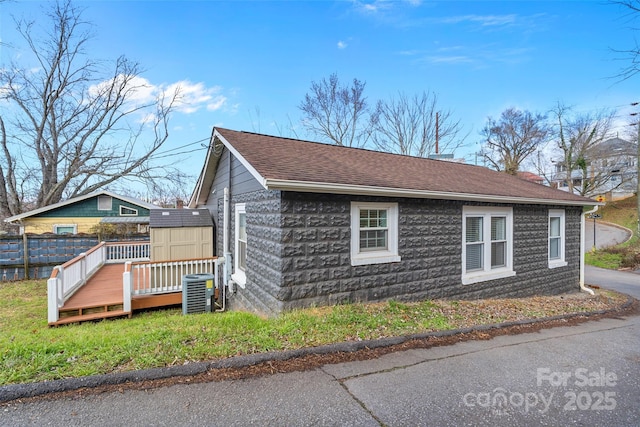 view of side of property with a wooden deck, central AC unit, and a storage unit