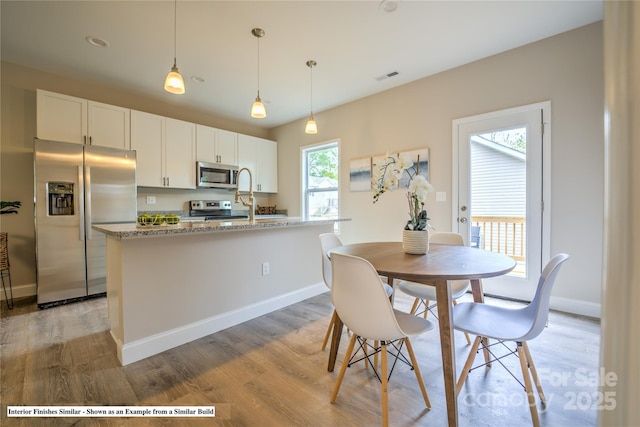 kitchen featuring stainless steel appliances, white cabinetry, baseboards, hanging light fixtures, and light wood-type flooring