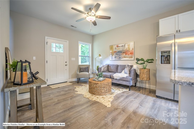 living area featuring light wood finished floors, baseboards, visible vents, and a ceiling fan