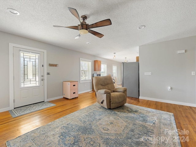 living room with ceiling fan, light hardwood / wood-style floors, and a textured ceiling