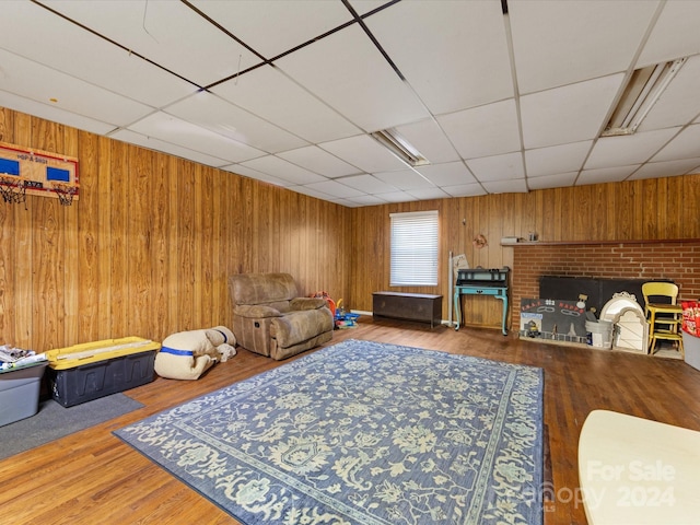 living room featuring a drop ceiling, wood-type flooring, a fireplace, and wooden walls