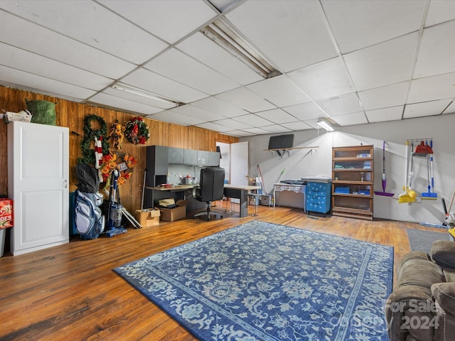 living room featuring hardwood / wood-style floors, a paneled ceiling, and wooden walls