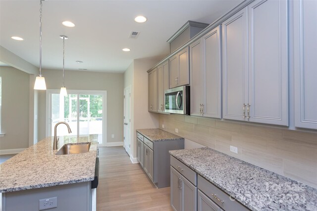 kitchen featuring light stone countertops, backsplash, sink, pendant lighting, and an island with sink