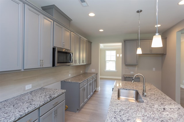 kitchen featuring backsplash, sink, hanging light fixtures, gray cabinets, and light stone counters