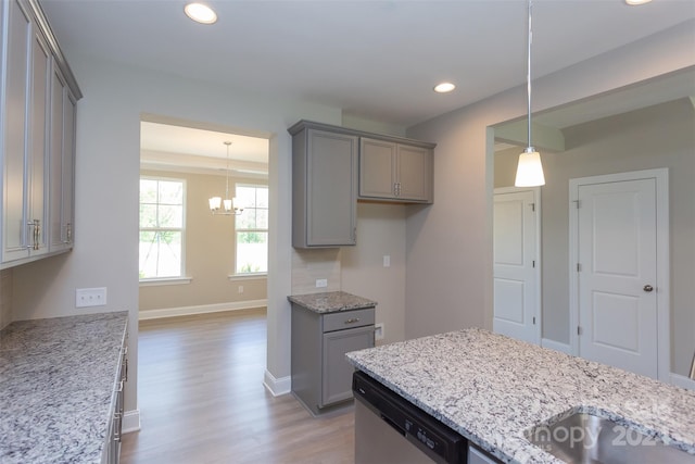 kitchen featuring pendant lighting, light hardwood / wood-style flooring, stainless steel dishwasher, a notable chandelier, and light stone counters