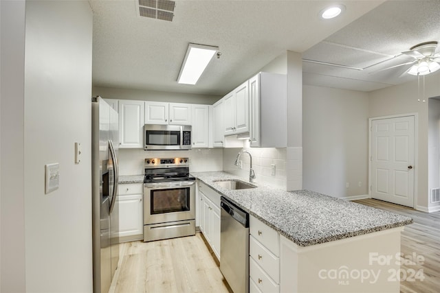 kitchen featuring white cabinetry, sink, light stone counters, kitchen peninsula, and appliances with stainless steel finishes