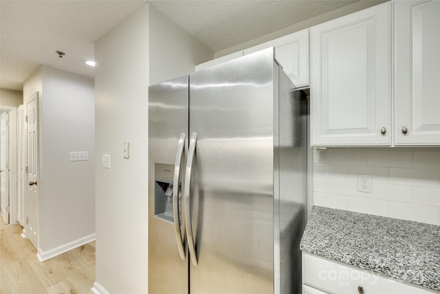 kitchen featuring stainless steel refrigerator with ice dispenser, backsplash, light stone counters, light hardwood / wood-style floors, and white cabinetry