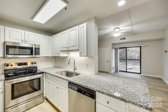 kitchen with white cabinets, sink, light stone countertops, appliances with stainless steel finishes, and light hardwood / wood-style floors