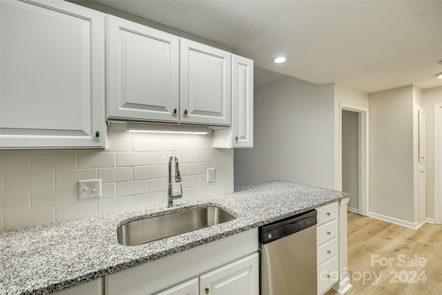 kitchen with light stone counters, stainless steel dishwasher, sink, light hardwood / wood-style floors, and white cabinetry