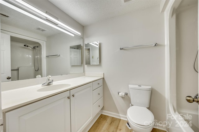 bathroom featuring vanity, hardwood / wood-style flooring, toilet, a textured ceiling, and walk in shower