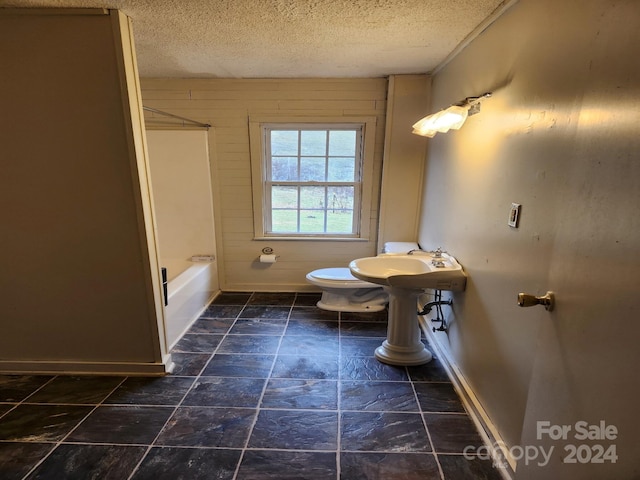 full bathroom featuring wooden walls, sink, a textured ceiling, and toilet