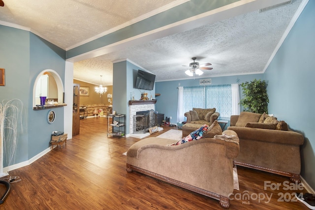 living room featuring ornamental molding, ceiling fan with notable chandelier, a textured ceiling, hardwood / wood-style flooring, and a stone fireplace