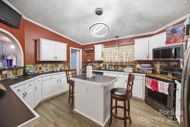 kitchen featuring a kitchen bar, white cabinets, decorative light fixtures, and appliances with stainless steel finishes