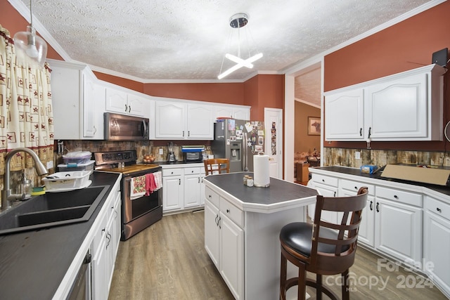 kitchen featuring stainless steel appliances, sink, decorative light fixtures, white cabinets, and a center island