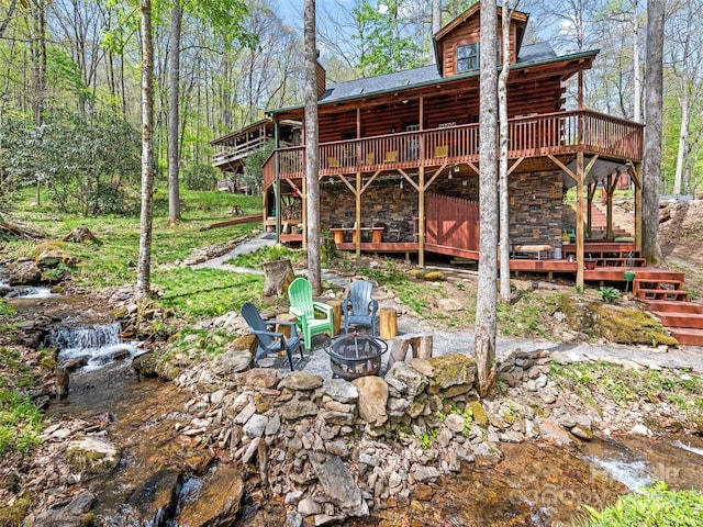 rear view of house featuring a deck with water view and a fire pit