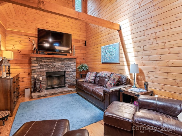 living room featuring high vaulted ceiling, hardwood / wood-style flooring, a stone fireplace, and wood walls