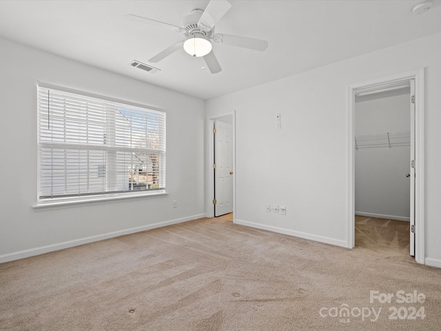 unfurnished bedroom featuring a closet, light colored carpet, a spacious closet, and ceiling fan