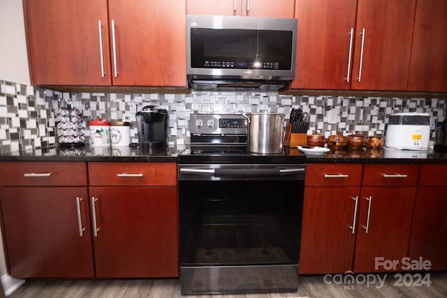 kitchen featuring dark stone countertops, light wood-type flooring, backsplash, and appliances with stainless steel finishes