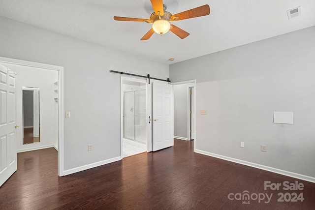 unfurnished bedroom featuring ceiling fan, a barn door, dark wood-type flooring, and ensuite bath