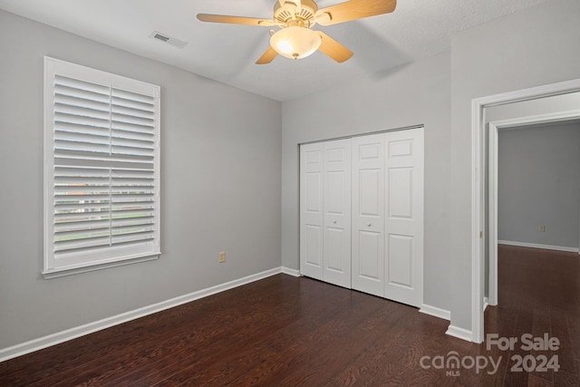 unfurnished bedroom with a textured ceiling, ceiling fan, dark wood-type flooring, and a closet