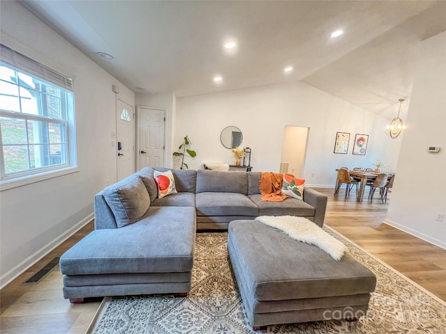 living room with visible vents, an inviting chandelier, wood finished floors, baseboards, and vaulted ceiling