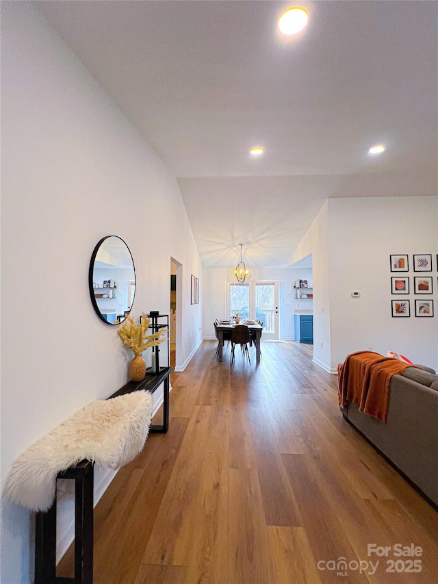 hall with vaulted ceiling, a notable chandelier, baseboards, and light wood finished floors