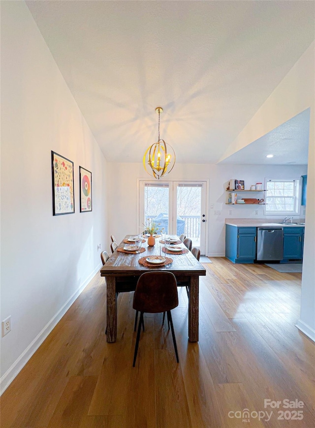 dining room featuring baseboards, a chandelier, vaulted ceiling, and light wood-style floors