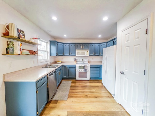 kitchen with blue cabinetry, a sink, light countertops, light wood-style floors, and white appliances