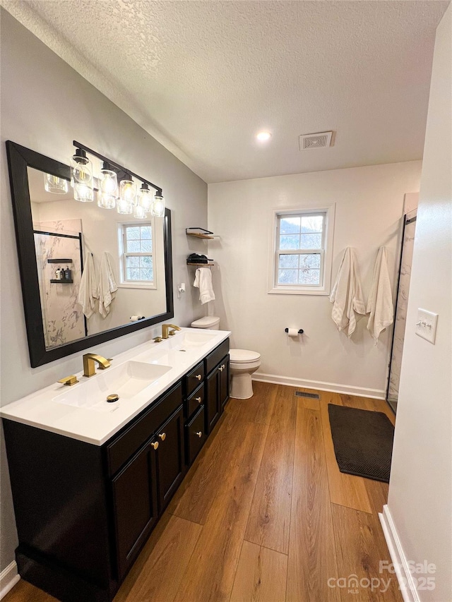 full bathroom with a sink, toilet, a textured ceiling, wood finished floors, and visible vents