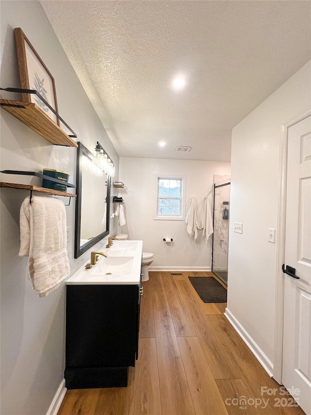 full bathroom with vanity, wood finished floors, toilet, a textured ceiling, and an enclosed shower