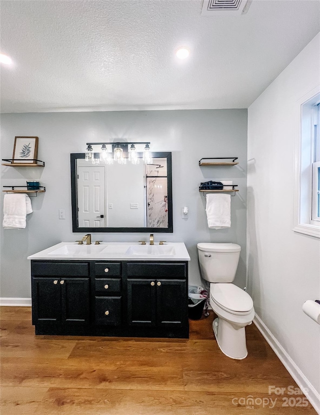 full bathroom featuring a sink, double vanity, toilet, baseboards, and wood finished floors
