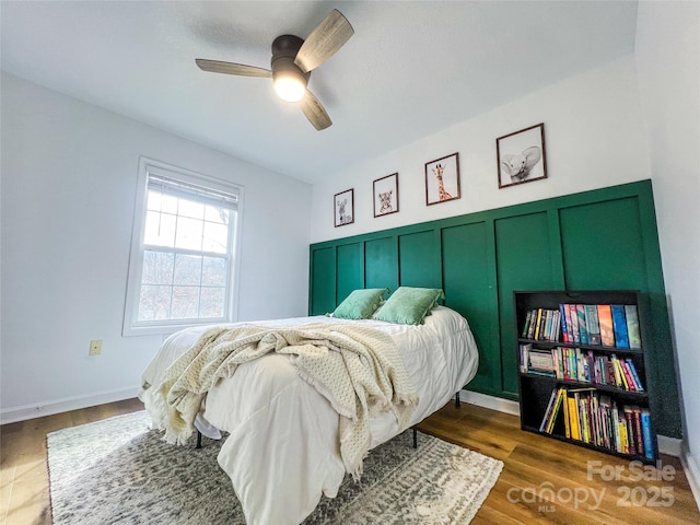 bedroom with dark wood-type flooring, a ceiling fan, and wainscoting