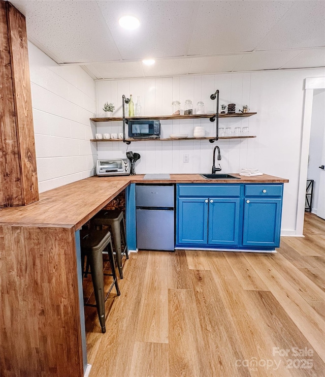 bar with a sink, light wood-style flooring, a drop ceiling, and black microwave