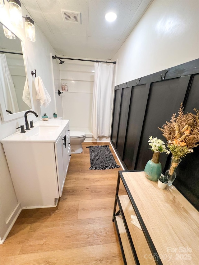 bathroom with a shower with curtain, visible vents, wood finished floors, vanity, and toilet