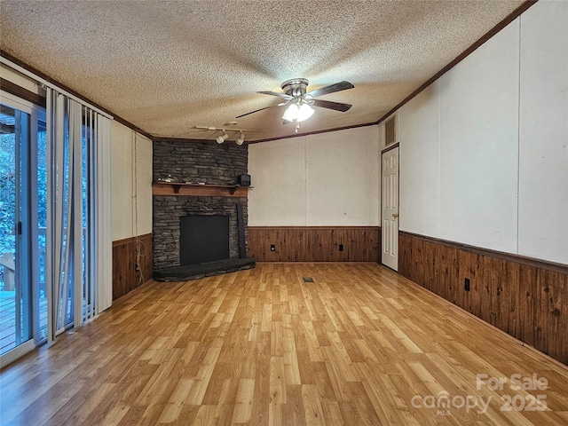 unfurnished living room featuring a textured ceiling, ornamental molding, wooden walls, a fireplace, and light hardwood / wood-style floors