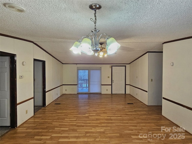 spare room with ornamental molding, light hardwood / wood-style floors, a textured ceiling, and a notable chandelier