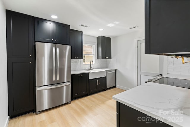 kitchen with visible vents, a sink, appliances with stainless steel finishes, dark cabinets, and light wood finished floors