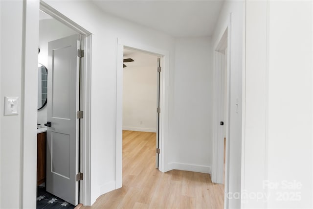 corridor featuring light wood-style flooring and baseboards