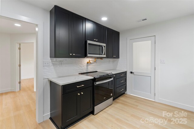 kitchen featuring stainless steel appliances, dark cabinets, and light wood-type flooring