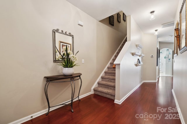 staircase with arched walkways, visible vents, baseboards, and wood finished floors