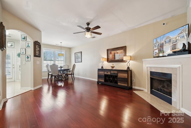 dining space featuring arched walkways, ceiling fan, a fireplace, wood finished floors, and baseboards