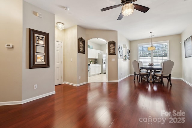 dining space featuring arched walkways, wood finished floors, a ceiling fan, and baseboards